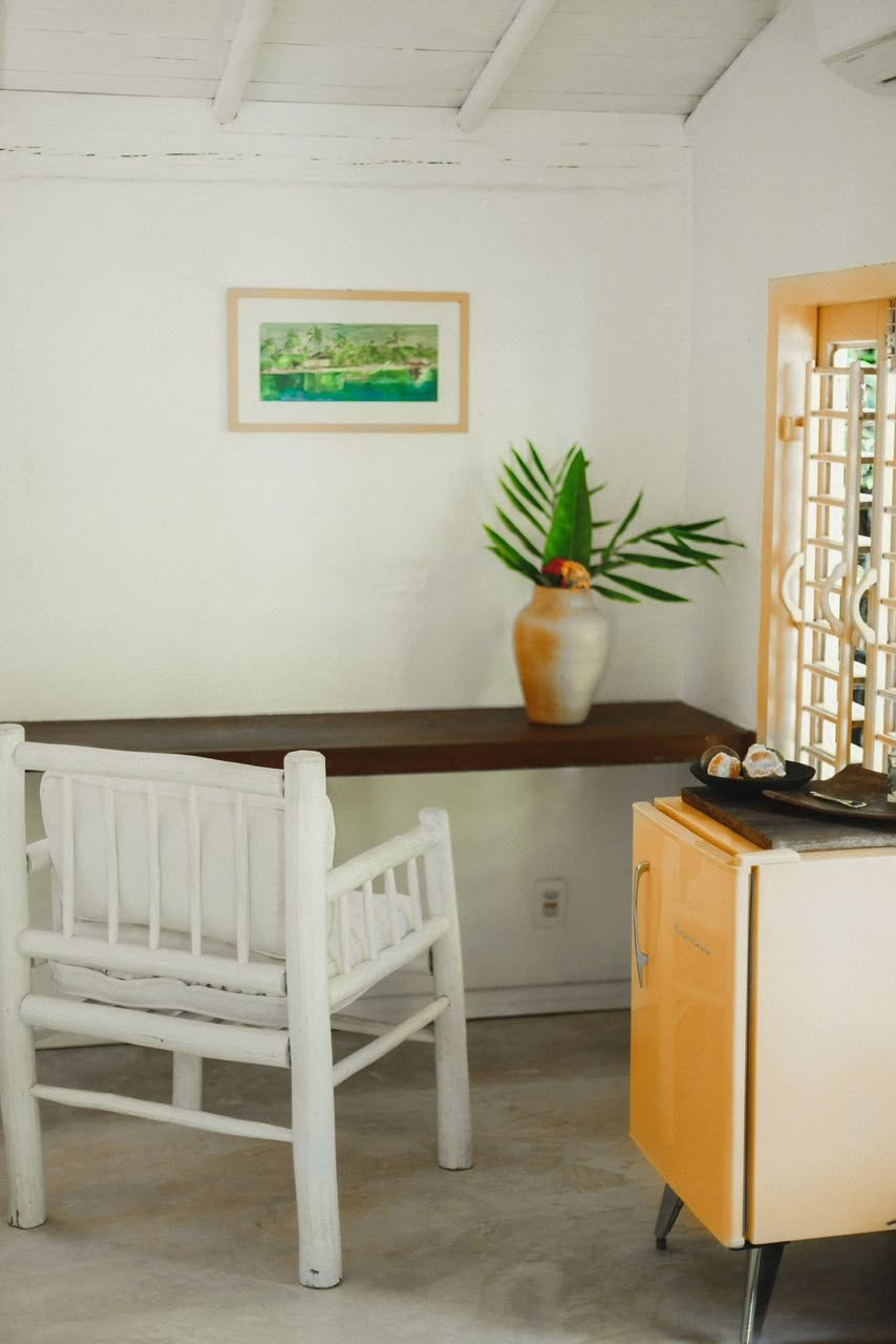 Cadeira branca e aparador com quadro e frigobar amarelo no Bangalô Amarelo