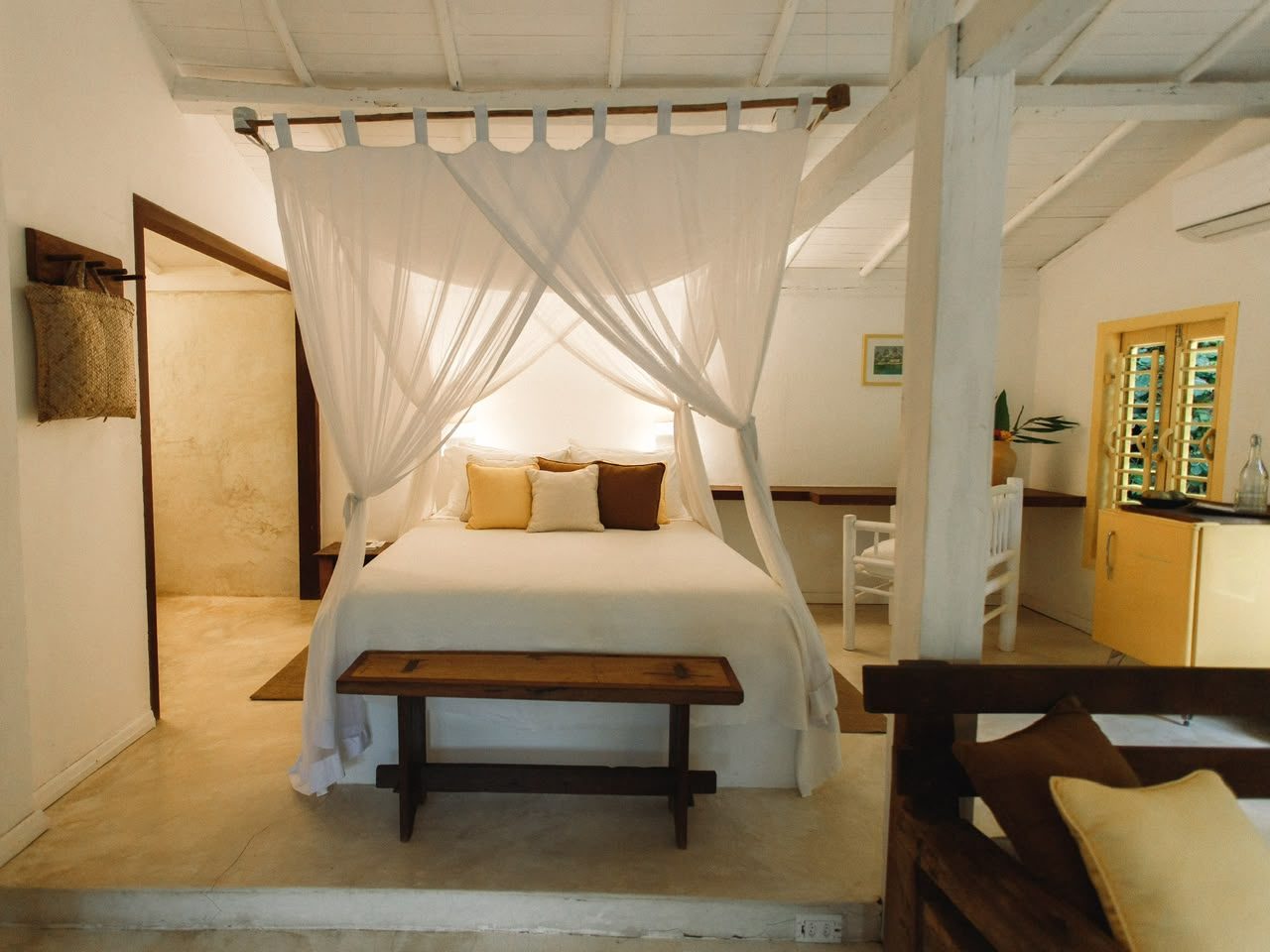 Quarto do Bangalô Amarelo com cama de dossel, banco de madeira e frigobar amarelo